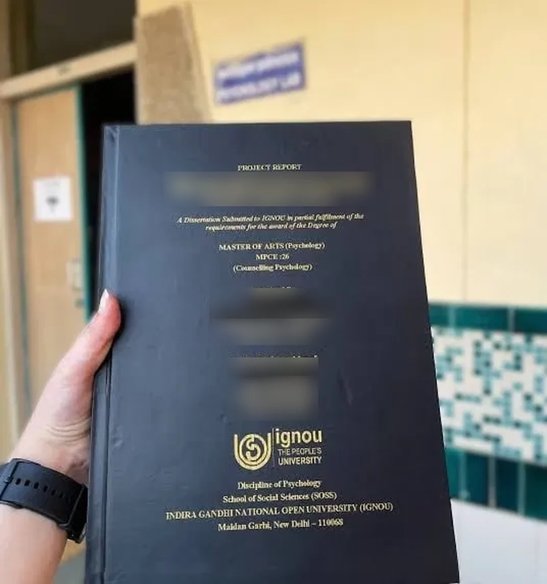 Hard-bound IGNOU project report cover held up, with the student and supervisor details blurred